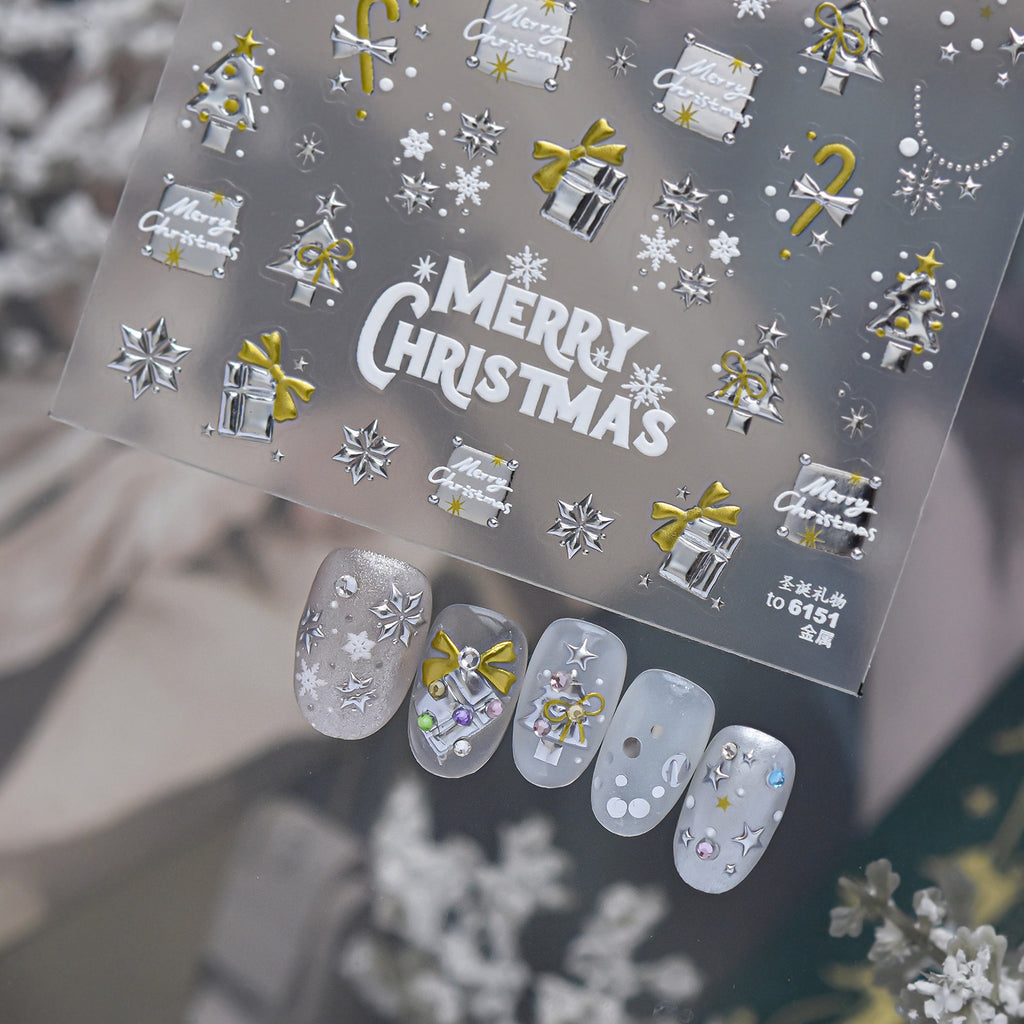 Detailed view of gold Christmas nail decals featuring intricate designs of snowflakes, reindeer, stars, wreaths, and "Merry Christmas" text on a clear backing, shown with elegant gold and white winter press-on nails.