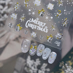 Detailed view of gold Christmas nail decals featuring intricate designs of snowflakes, reindeer, stars, wreaths, and "Merry Christmas" text on a clear backing, shown with elegant gold and white winter press-on nails.