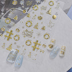 Detailed view of gold Christmas nail decals featuring intricate designs of snowflakes, reindeer, stars, wreaths, and "Merry Christmas" text on a clear backing, shown with elegant gold and white winter press-on nails.