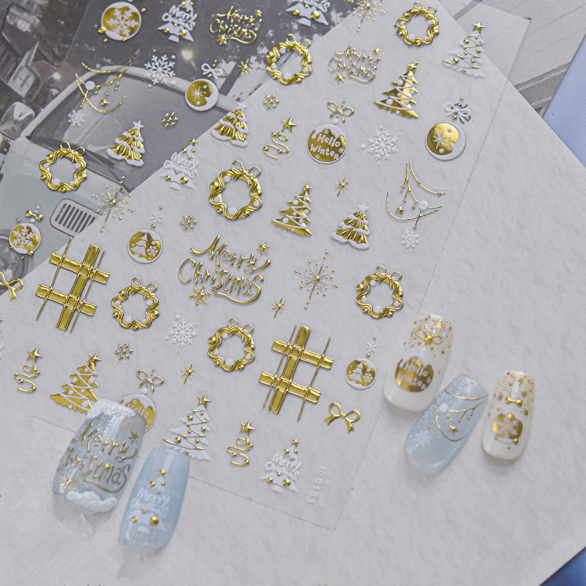 Detailed view of gold Christmas nail decals featuring intricate designs of snowflakes, reindeer, stars, wreaths, and "Merry Christmas" text on a clear backing, shown with elegant gold and white winter press-on nails.