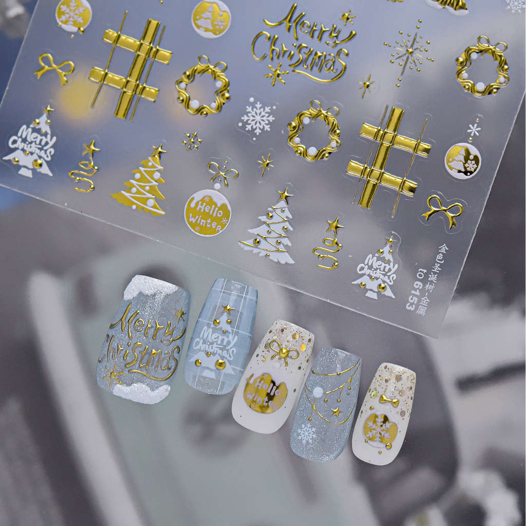 Detailed view of gold Christmas nail decals featuring intricate designs of snowflakes, reindeer, stars, wreaths, and "Merry Christmas" text on a clear backing, shown with elegant gold and white winter press-on nails.
