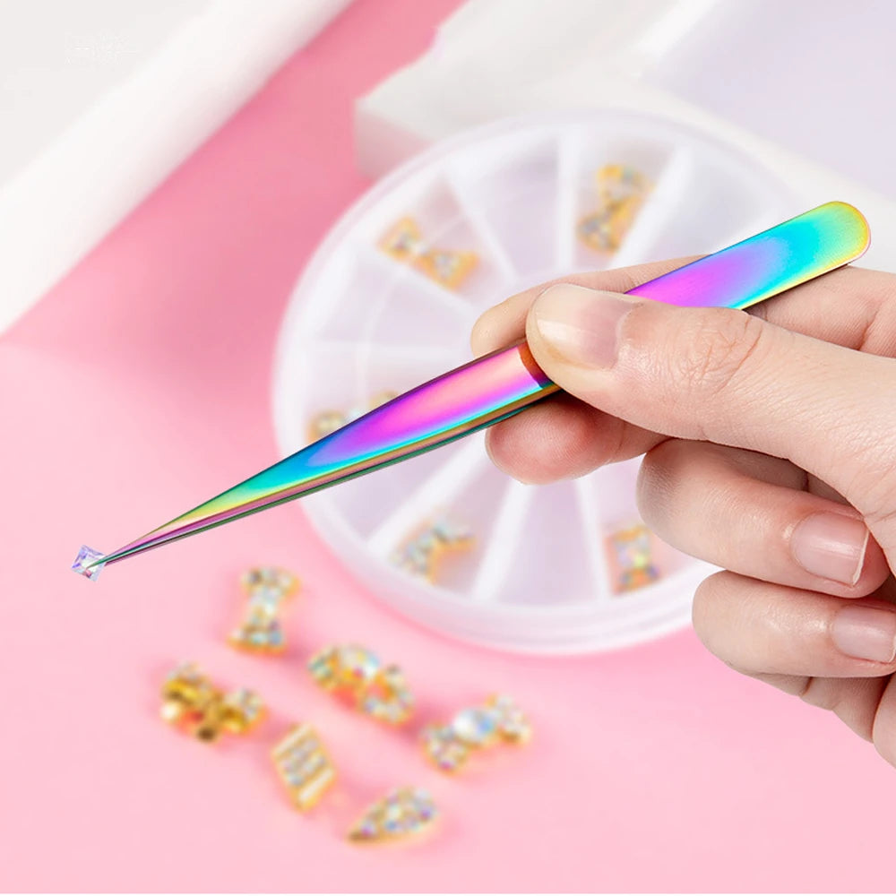 A person using a fine-point rainbow nail art tweezer to precisely pick up a small, sparkling rhinestone for a manicure.