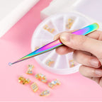 A person using a fine-point rainbow nail art tweezer to precisely pick up a small, sparkling rhinestone for a manicure.