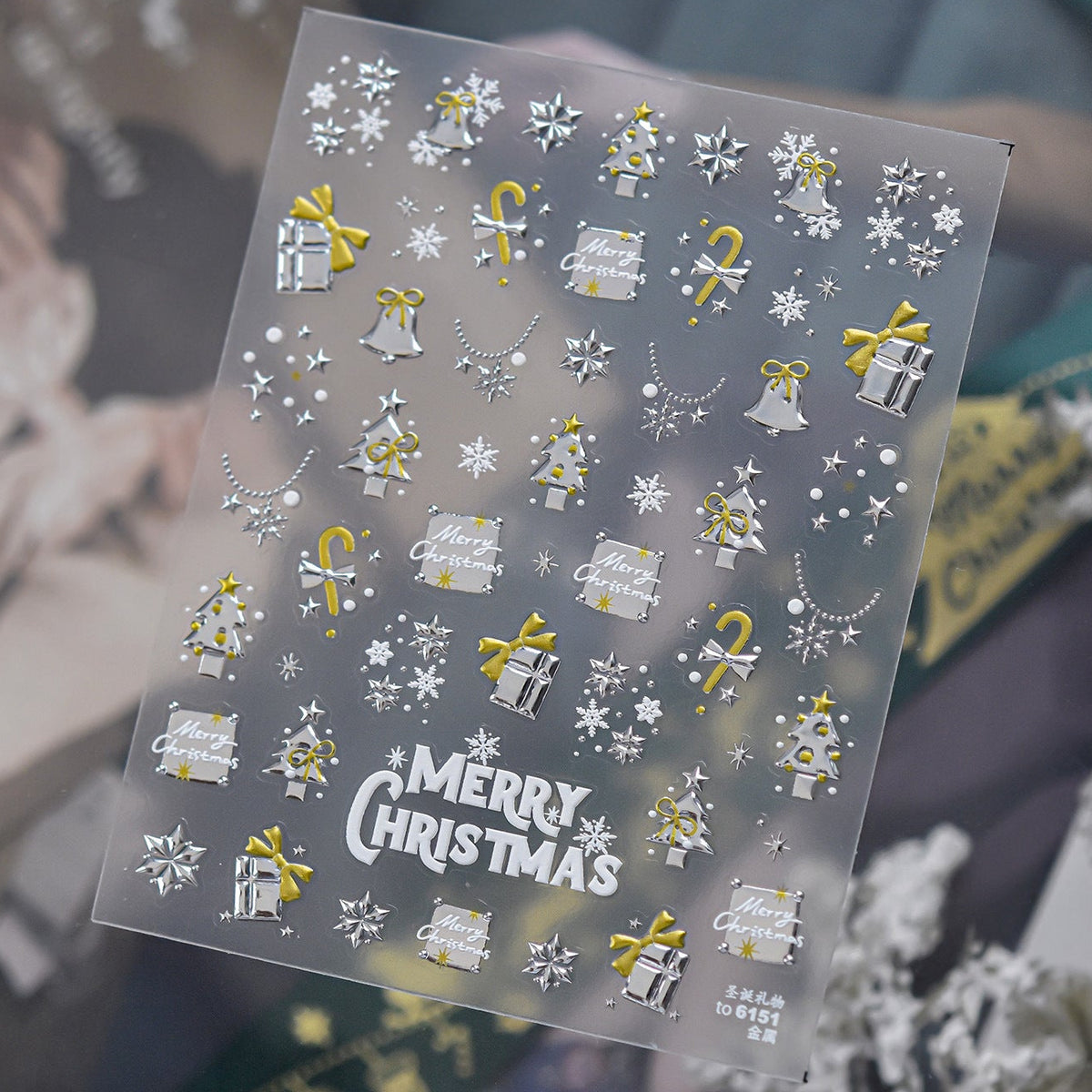Detailed view of gold Christmas nail decals featuring intricate designs of snowflakes, reindeer, stars, wreaths, and "Merry Christmas" text on a clear backing, shown with elegant gold and white winter press-on nails.
